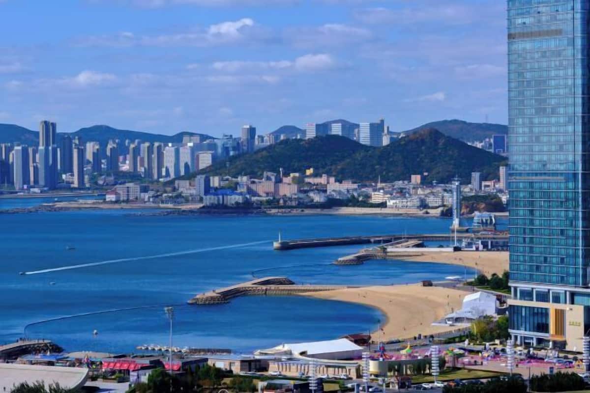 A coastal cityscape with a prominent modern skyscraper, a beach, and a marina.