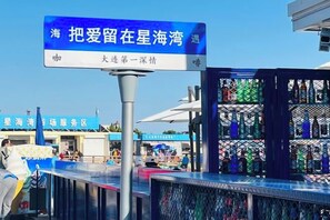 Un letrero con caracteres chinos, una zona de bar con botellas, y un edificio con un letrero azul al fondo.