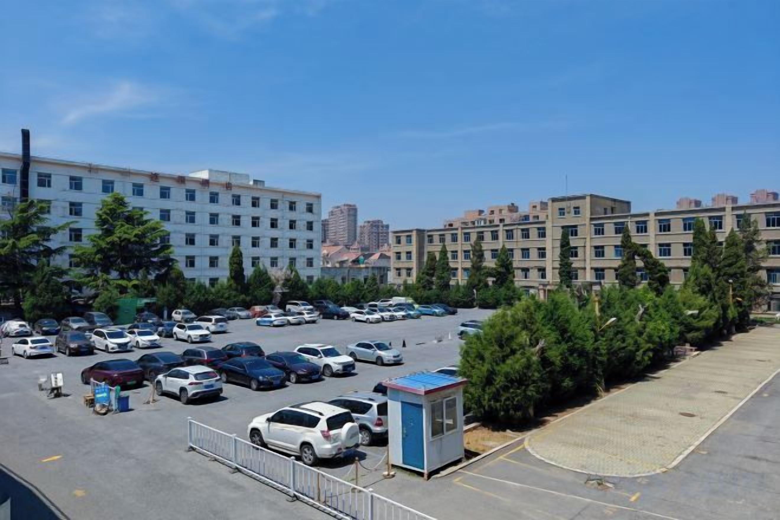 A parking lot with multiple cars, a small blue structure, and buildings in the background.