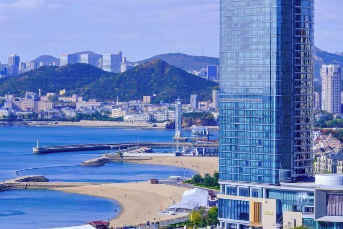 A coastal cityscape with a prominent modern glass skyscraper, a beach, and a hilly backdrop.