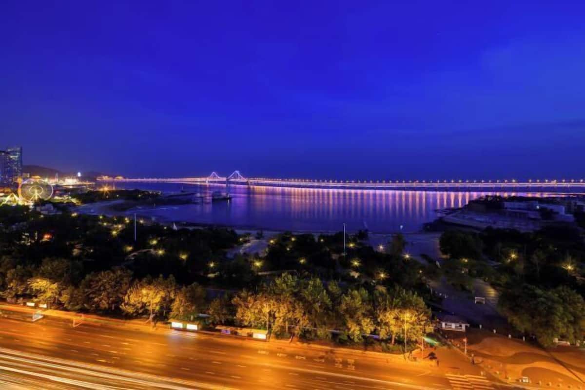 A nighttime view of a bridge over a body of water, with city lights reflecting on the surface.