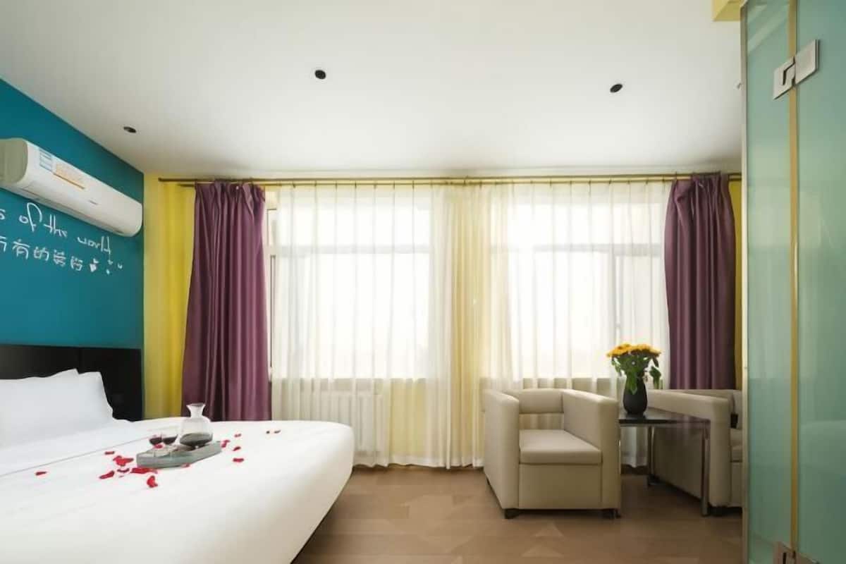 A hotel room with a bed, two chairs, a small table with a vase, and a window with curtains.