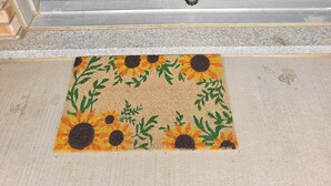 Une porte bleue avec deux poignées en laiton et un paillasson orné de tournesols.