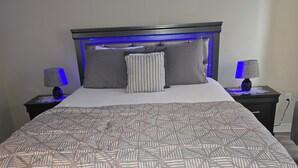 Un lit bien fait, recouvert d’une couvre-lit à motifs, avec deux lampes de chevet et une tête de lit dotée d’un éclairage bleu.