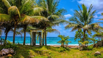 A tropical beach scene with palm trees, a stone structure, and the ocean.