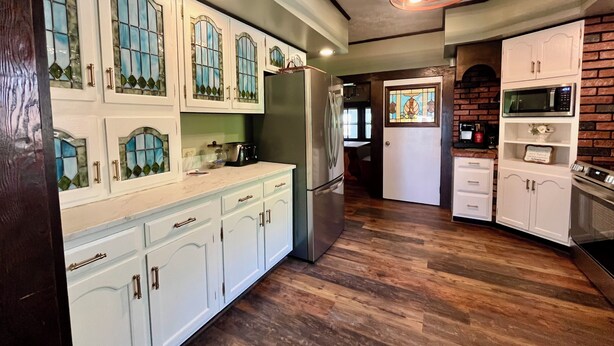 Una cocina con armarios blancos, un refrigerador, un microondas y piso de madera.