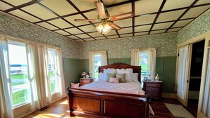 Un dormitorio con una cama de madera, un ventilador de techo y vistas a un jardín verde a través de la ventana.
