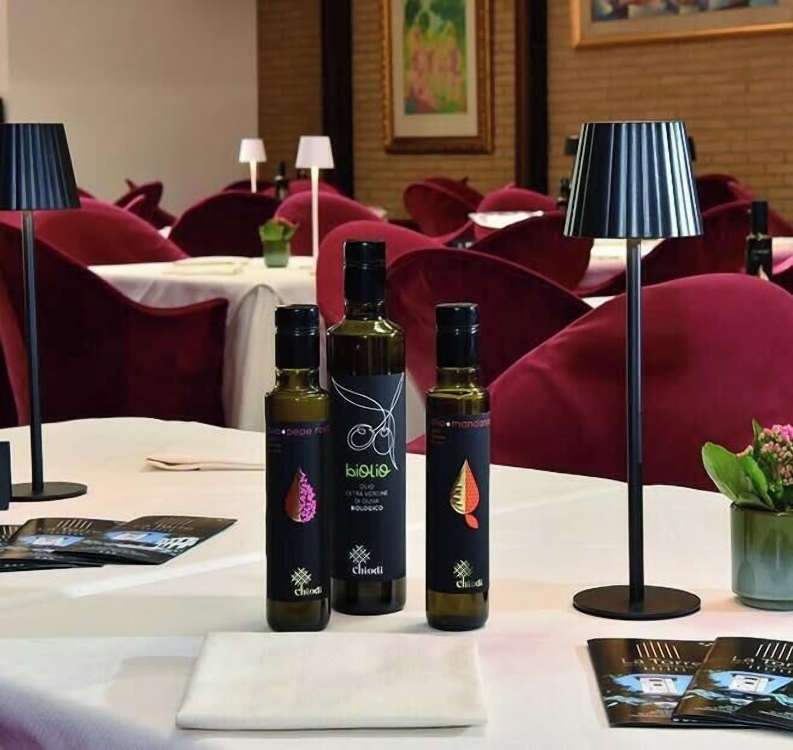 Une chambre d’hôtel avec une table à manger dressée pour deux personnes, deux bouteilles de vin et une lampe.