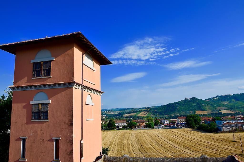 A pink tower with arched windows overlooking a field and a village.