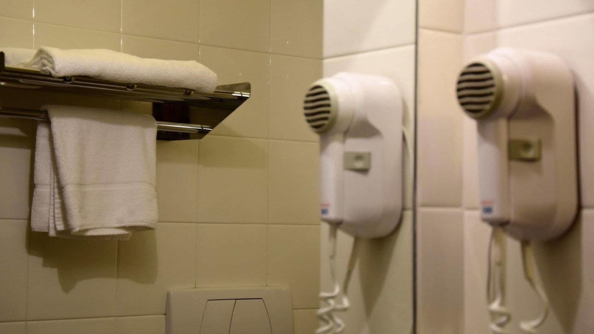 Un baño con azulejos blancos, un perchero con toallas dobladas y dos secadores de pelo fijados a la pared.