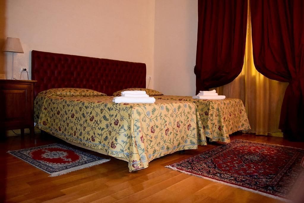 Una cama doble con ropa de cama floral, dos almohadas y una mesita de noche con una lámpara.