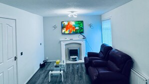 A living room with a fireplace, a mounted TV, and a ceiling light fixture. - Gateshead Gem - Modern 3 Bedroom House (Gateshead)
