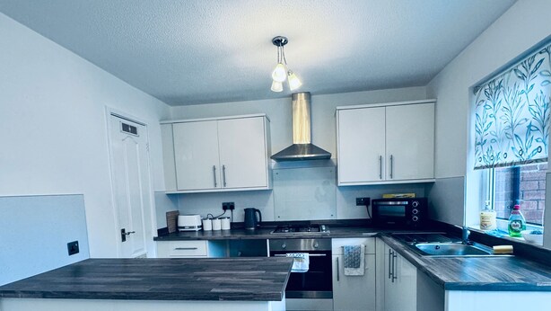 A modern kitchen with white cabinets, a central island, a stove, and a microwave. - Gateshead Gem - Modern 3 Bedroom House (Gateshead)