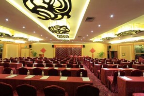 Un salón de conferencias con mesas y sillas dispuestas en filas, un escenario y un techo decorativo.