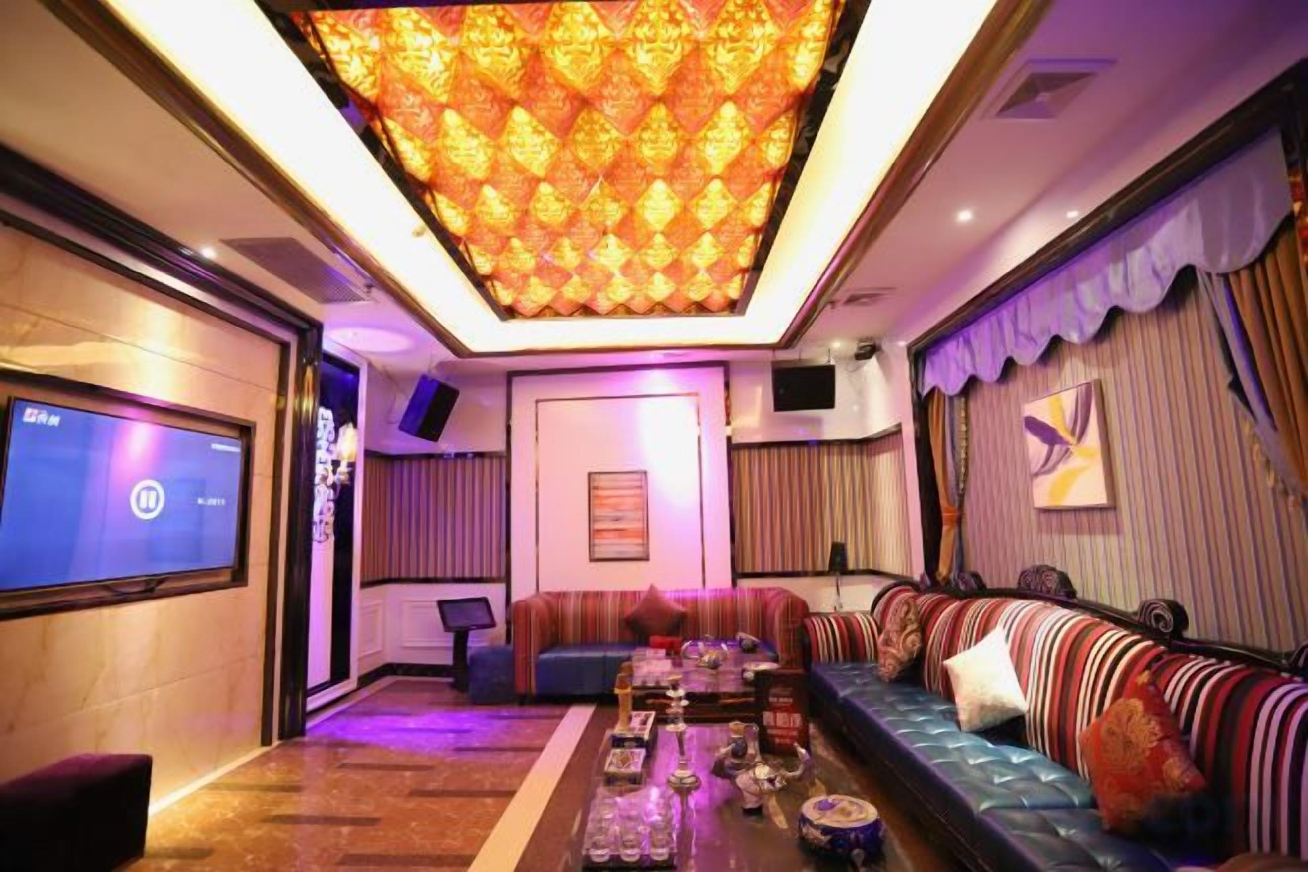 A modern living room with a large flat-screen TV, a patterned ceiling, and a sofa with cushions.
