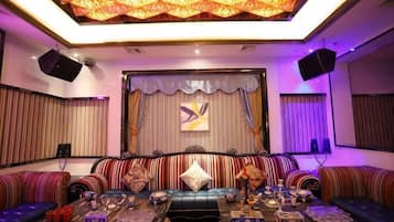 A room with a patterned ceiling, a stage with curtains, and a seating area with couches and a coffee table.
