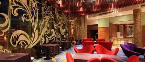 A hotel lobby with ornate wall designs, multiple seating areas, and a bar in the background.