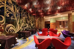 Um hall de hotel com designs de parede elaborados, várias áreas de estar e um bar ao fundo.