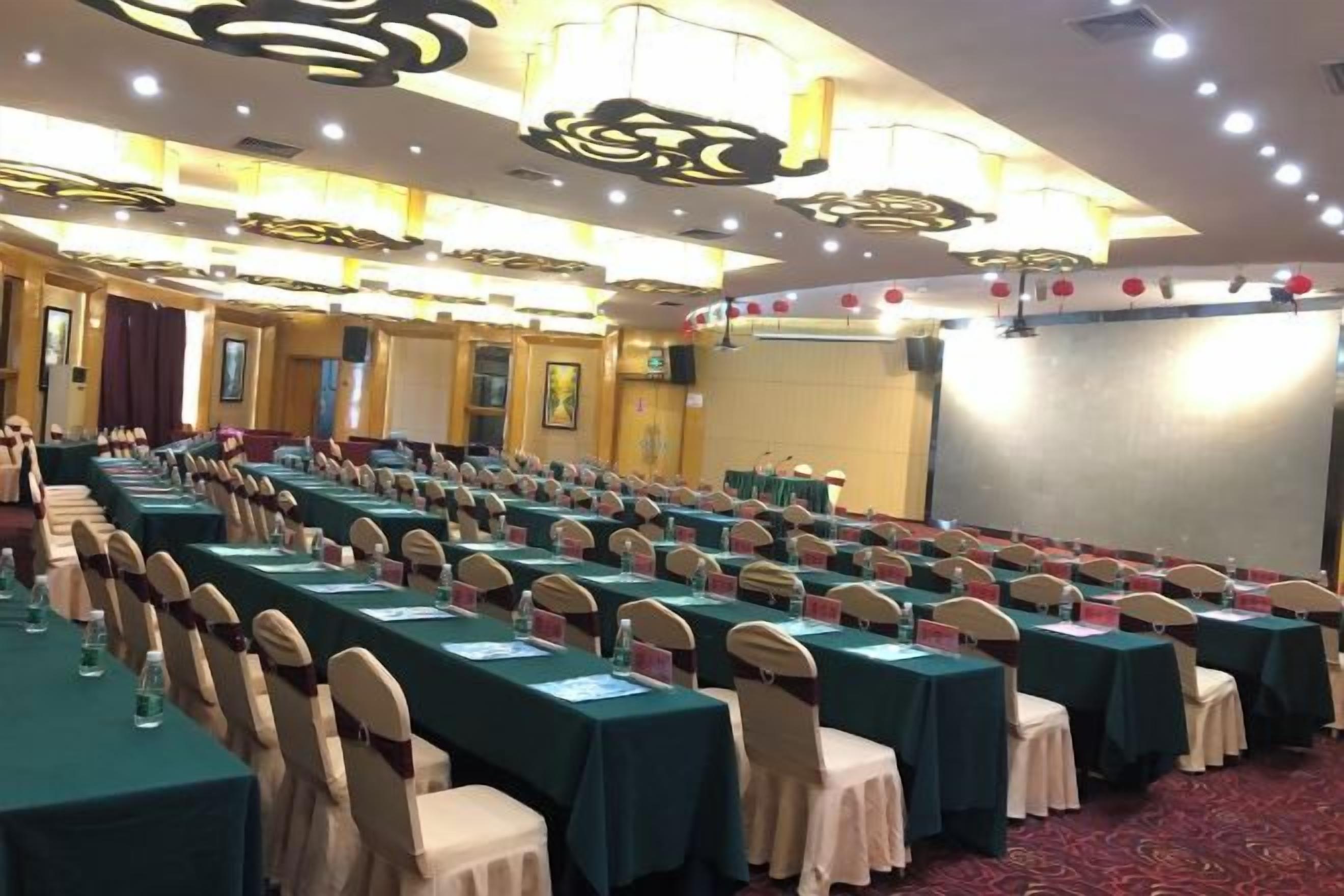A conference room with rows of tables and chairs, a stage, and a large screen.