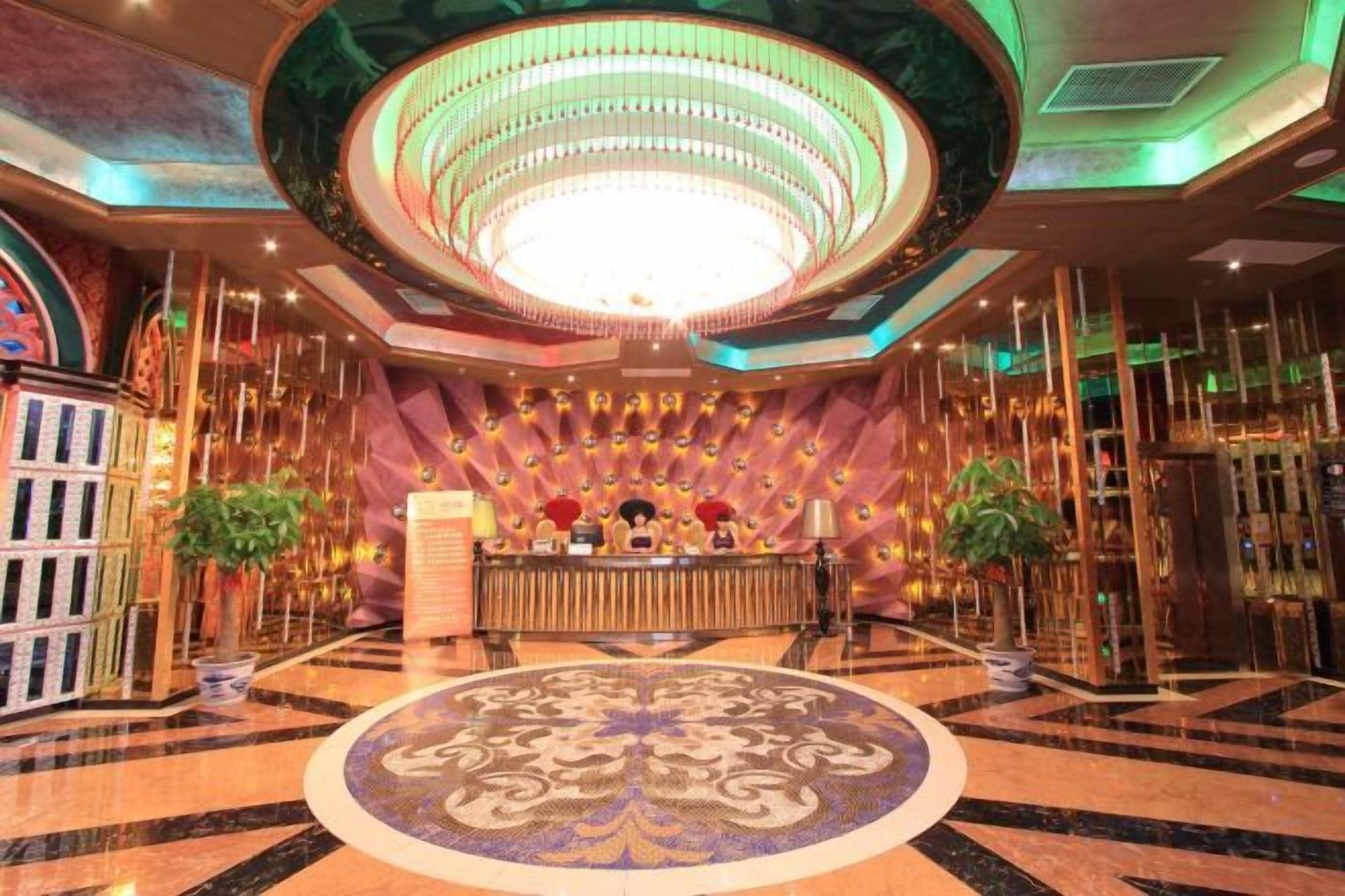 Un hall d’entrée doté d’un grand tapis rond orné de motifs, d’un comptoir de réception et d’un lustre.