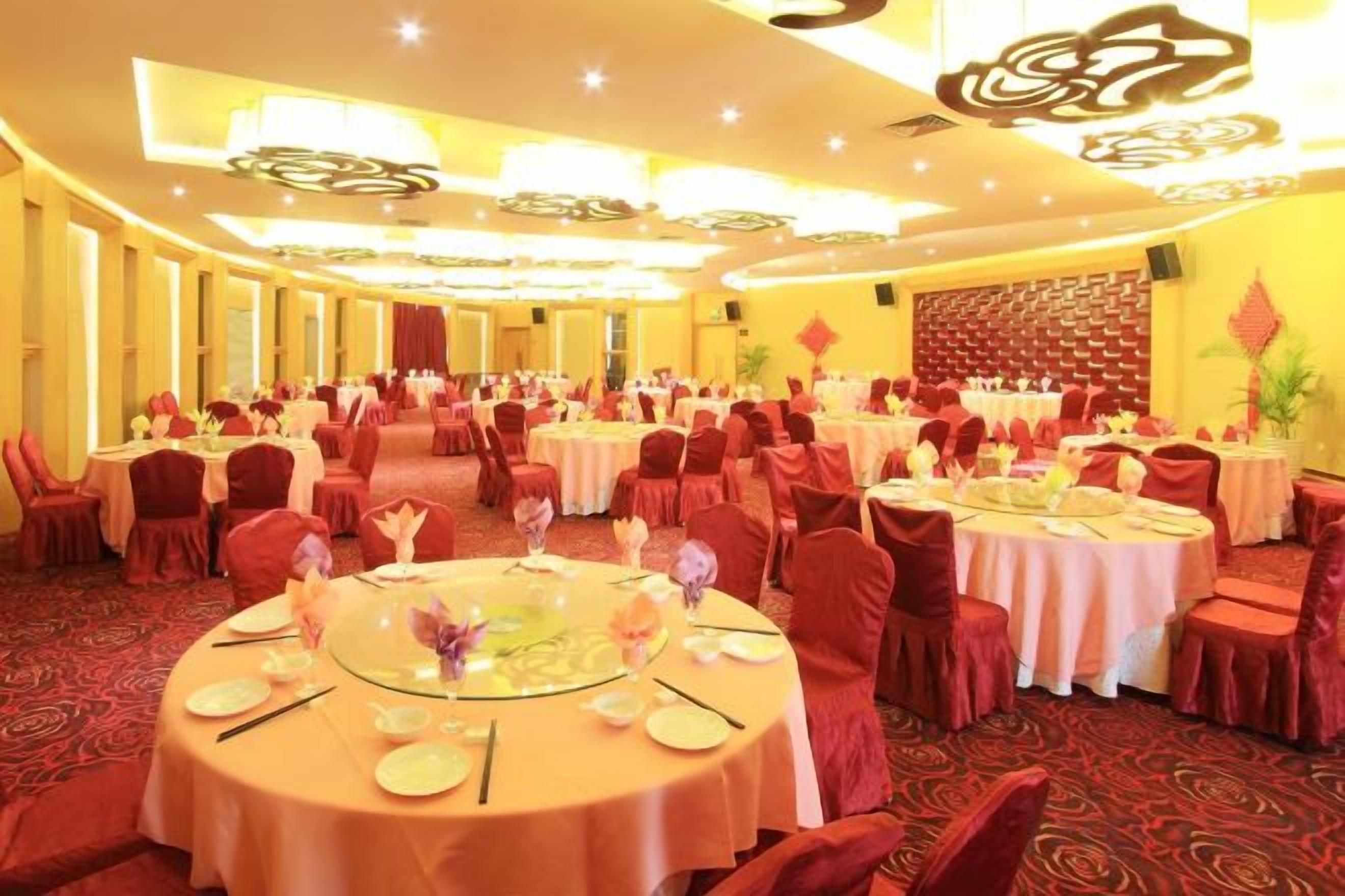 Un salón de banquetes con mesas redondas dispuestas para comer, sillas rojas y una alfombra estampada.