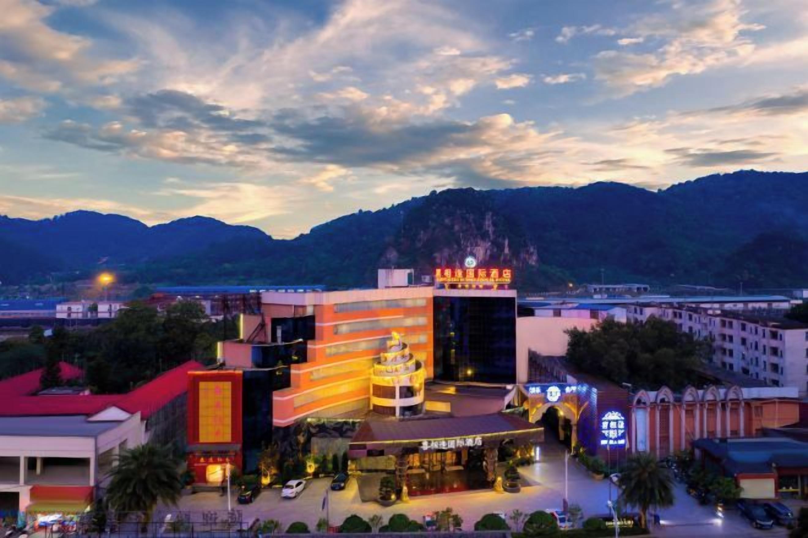 A hotel with a prominent sign, a parking area, and a mountainous backdrop.