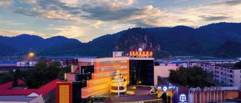 A hotel with a prominent sign, a parking area, and a mountainous backdrop.
