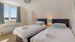 A bedroom with two beds, a window with curtains, a radiator, and a ceiling light fixture.