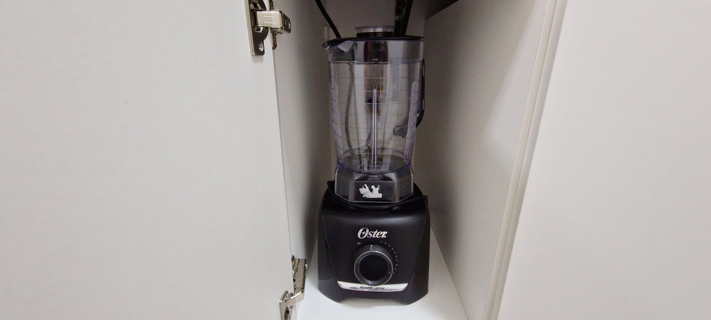 En sort Oster blender med en gennemsigtig beholder, monteret på en hvid væg.