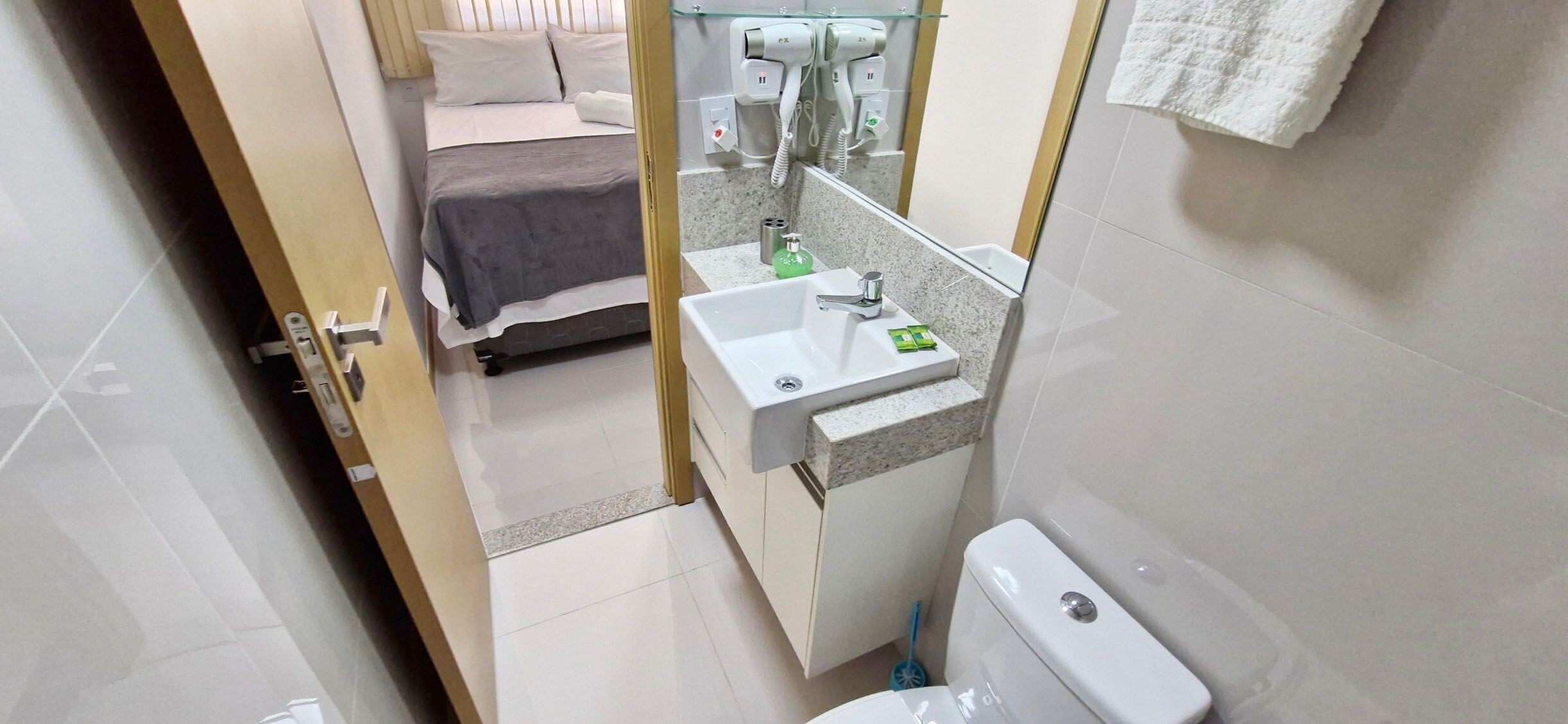 A hotel room with a bed, a bathroom with a sink, mirror, and toilet.
