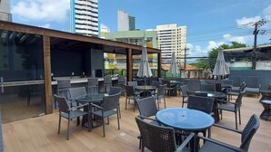 Un patio exterior con mobiliario de mimbre y una zona junto a la piscina, con vistas a un paisaje urbano con edificios altos.