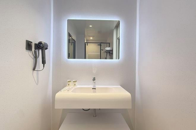 A bathroom with a white sink, a mirror, and a hairdryer mounted on the wall.