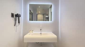 A bathroom with a white sink, a mirror, and a hairdryer mounted on the wall.