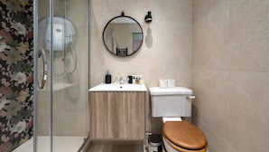 Ein Badezimmer mit Duschkabine aus Glas, Waschtisch aus Holz, Toilette und rundem Spiegel.
