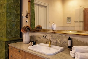 A bathroom with a marble sink, a gold faucet, a large mirror, a green cabinet, and a vase with dried flowers.