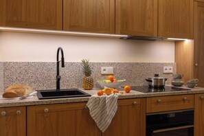 A kitchen with wooden cabinets, a granite countertop, a stainless steel sink, a stove, and a bowl of fruit.