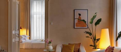A hotel room with a bed, a sitting area with a sofa and armchairs, a coffee table, a side table, a lamp, and a painting on the wall.