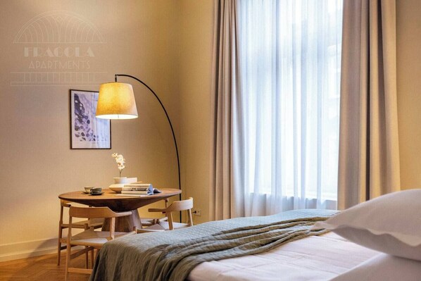 Une chambre d’hôtel avec un lit, un bureau doté d’une lampe, un tableau encadré et une fenêtre avec des rideaux.