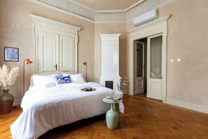 A bedroom with a large bed, a vase, a small table, and a door leading to another room.