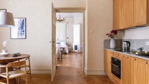 A hallway leading to a bedroom with a bed, a dining area with a table and chairs, and a kitchen with wooden cabinets and a countertop.