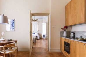 Um corredor dá acesso a um quarto com cama, uma área de refeições com mesa e cadeiras, e uma cozinha com armários de madeira e bancada.