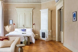 Un dormitorio con cama, mesitas de noche, chimenea y puerta.