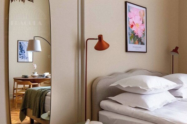 A hotel room with a bed, a desk with a lamp, a framed picture, and a mirror.