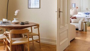 A room with a wooden dining table, chairs, a vase with flowers, and a bed with white bedding.