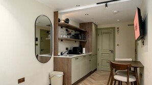 A compact kitchenette with a mirror, wooden cabinets, and a small dining area with a chair. - GuestReady - Chic studio in Euston (London)