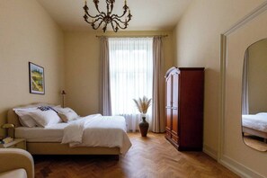 A bedroom with a bed, a wardrobe, a mirror, a chandelier, and a window with curtains. - Le Jardin Crème apartment (Kraków - Le Jardin)