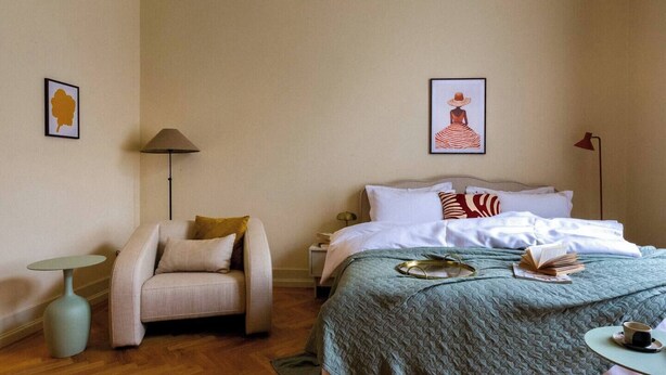 Ett hotellrum med en säng, en stol, ett litet bord och två väggmonterade lampor.