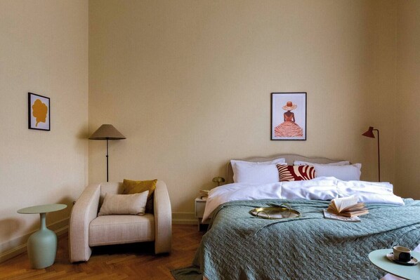 A hotel room with a bed, a chair, a small table, and two wall-mounted lamps.
