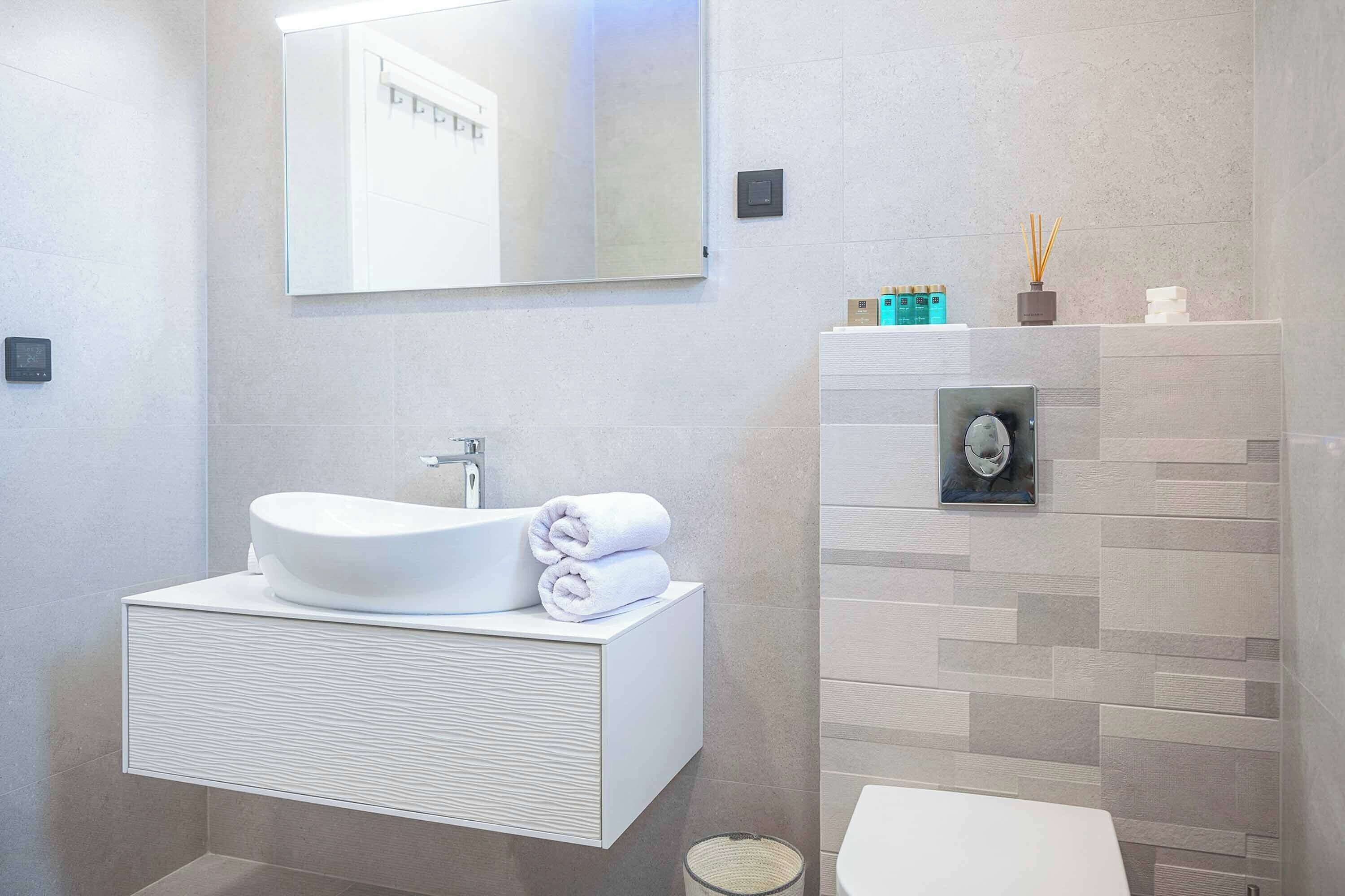 Un baño moderno con un lavamanos grande, un espejo y un inodoro de pared.