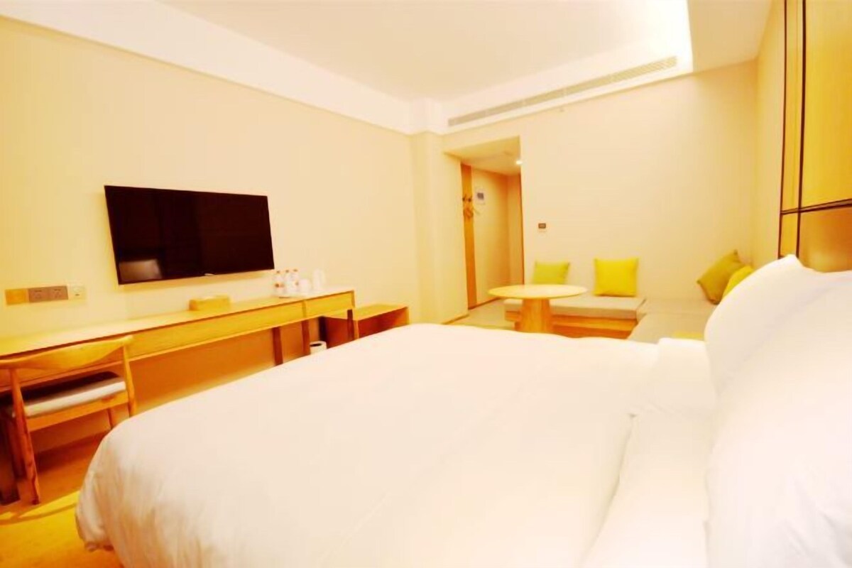 Habitación de hotel con cama, escritorio, silla, televisor y una pequeña mesa con otra silla.